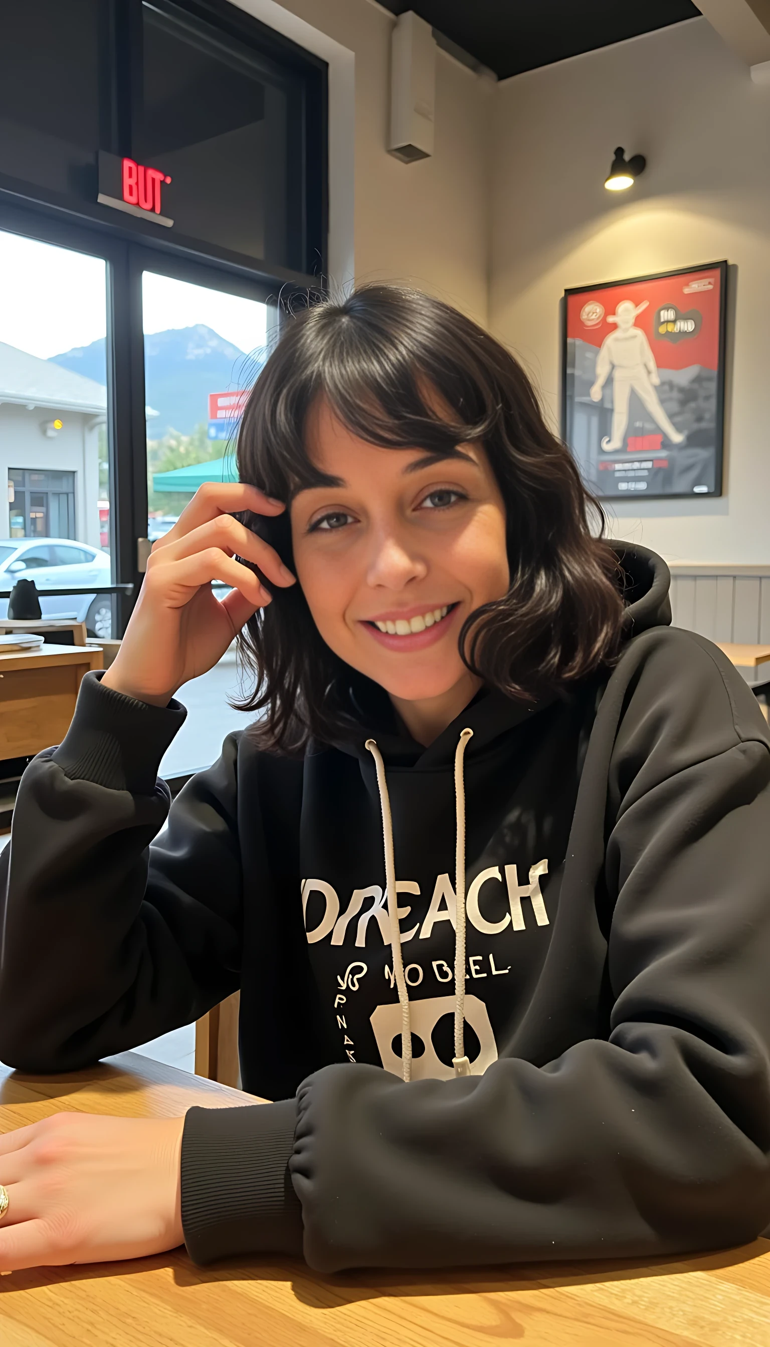 iphone portrait of CSTMDL woman younger Bob length hair hair makeup bangs cute smile brown eyes and sitting in cafe holding phone in busy restaurant wearing hoodie says “wizard”  mountains background shopping bags 
