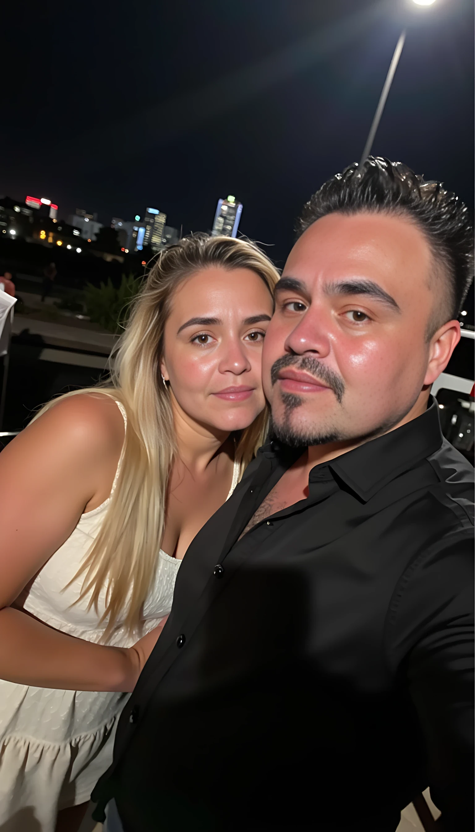 Selfie in a  mirror full man body wearing a  nice black dress shirt   Hugging with 1 blonde girl with blue eyes and 1 Mexican girl in a  big city night lights background 
