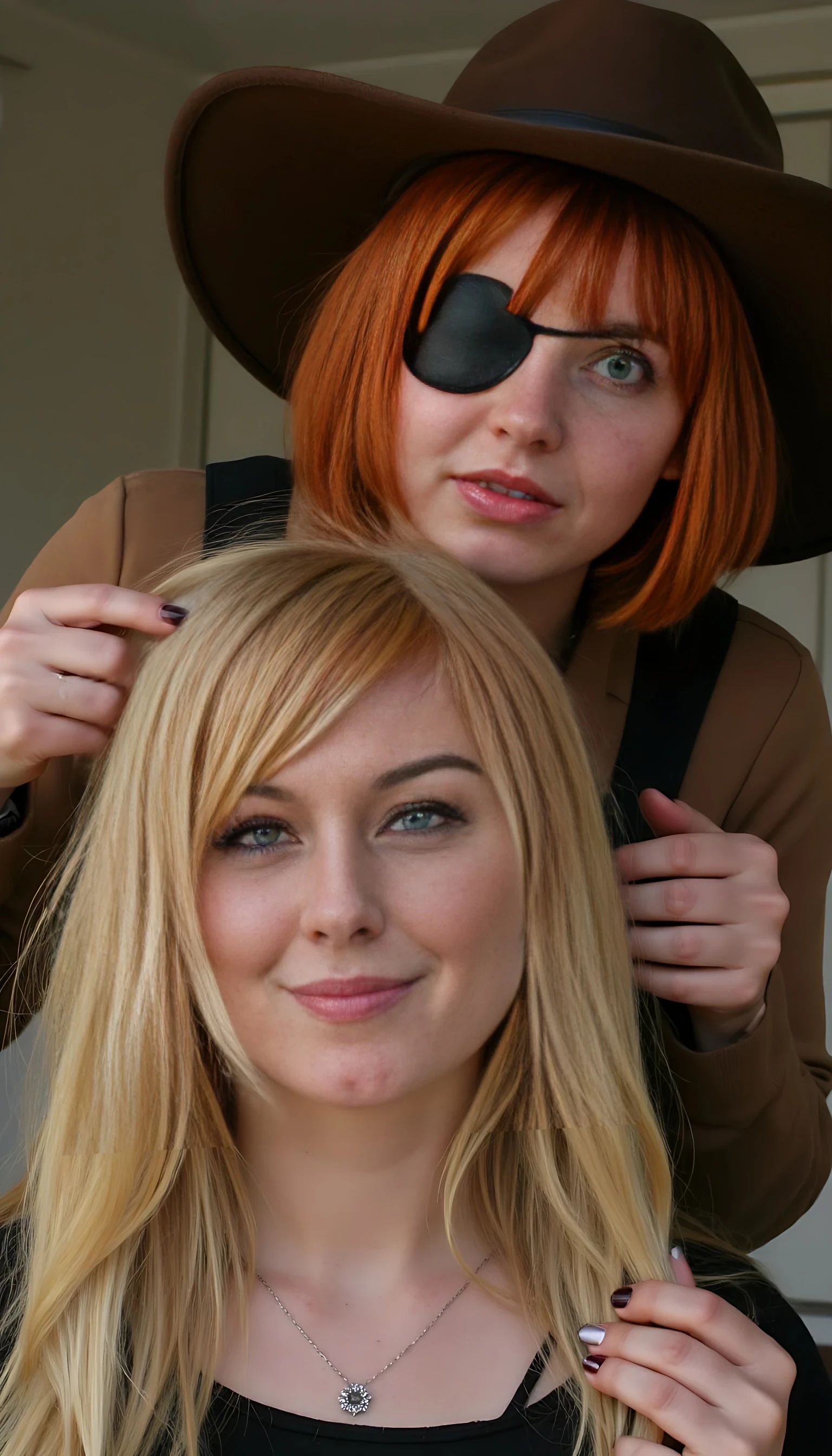 A short pixie style natural red head with a black eye patch over her left eye wearing a brown cowboy hat is playing with a blonde woman’s long blonde hair from behind holding it. The blonde is enjoying it. Highly realistic photo. 