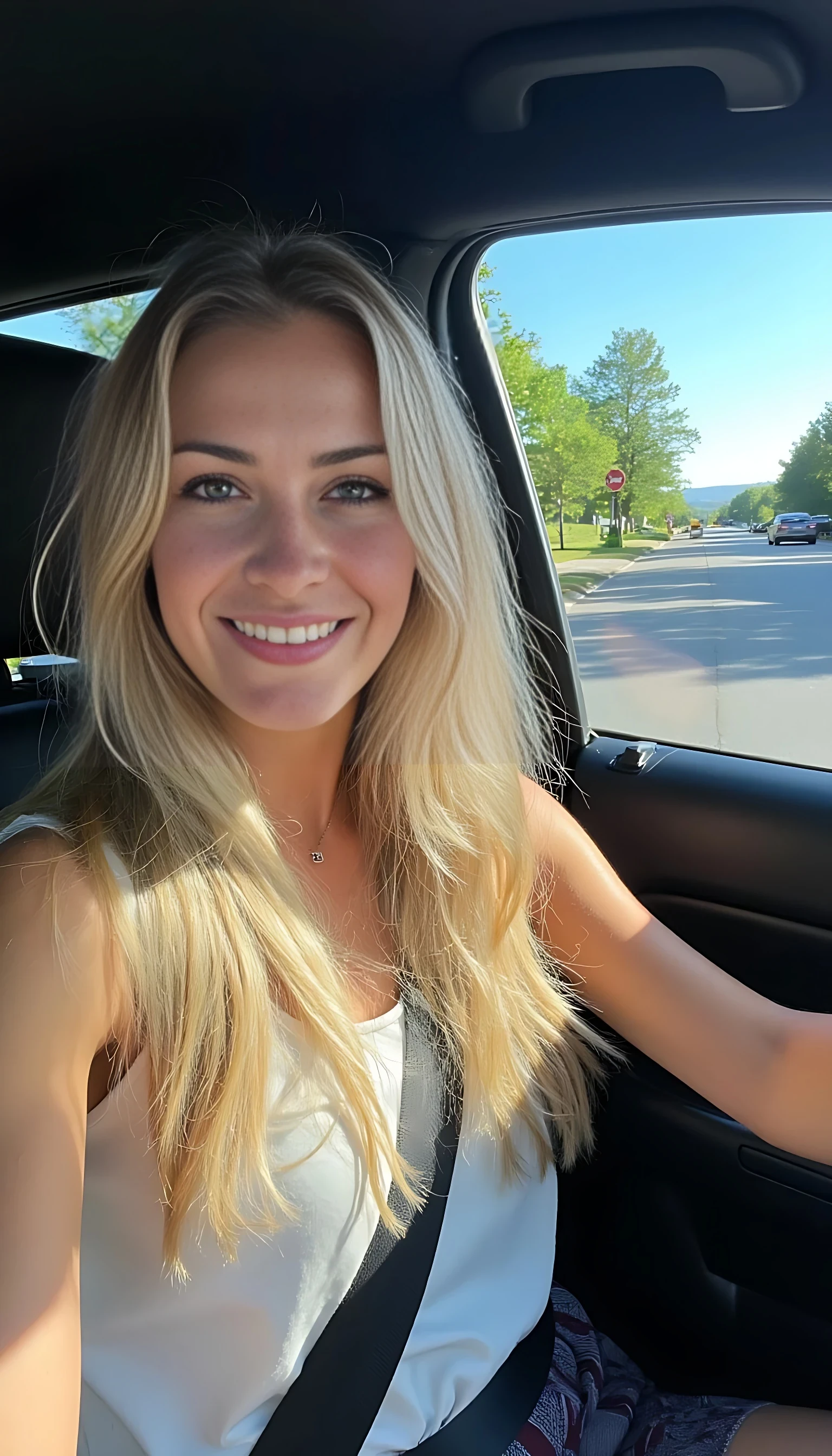boring low quality snapchat photo circa 2015, CSTMDL A young woman with a warm smile, sitting in the driver's seat of a cozy car. She has soft, long wavy blonde hair. The sunlight streams through the window, casting a gentle glow on her face. The interior of the car is neat and comfortable, with a coffee cup in the cup holder and a small plant on the dashboard. The background outside the window shows a scenic road lined with trees and blue skies