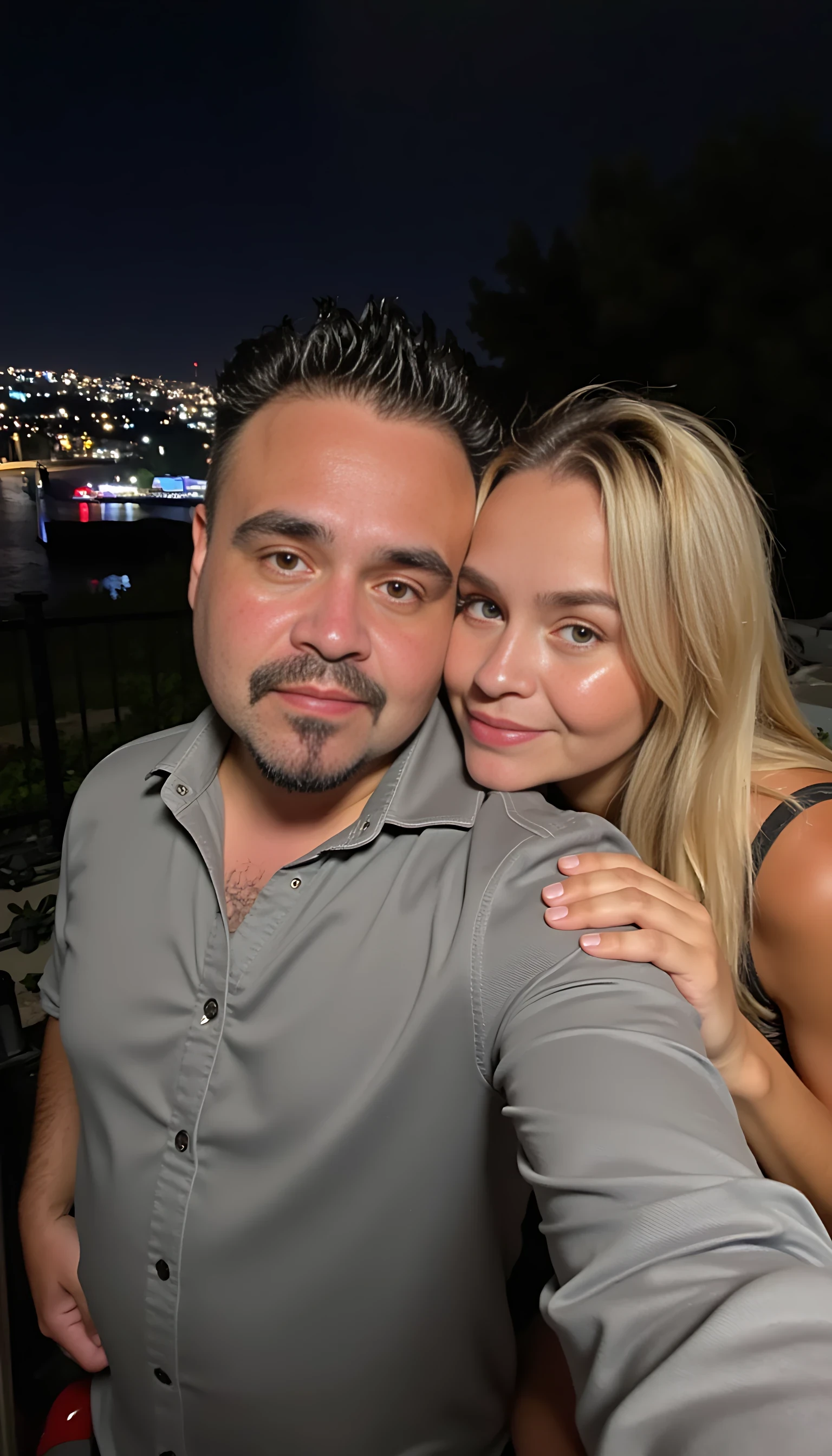 Selfie in a  mirror full man body wearing a  nice gray dress shirt   Hugging a beautiful blonde woman with blue eyes girl in a  big city night lights background 
