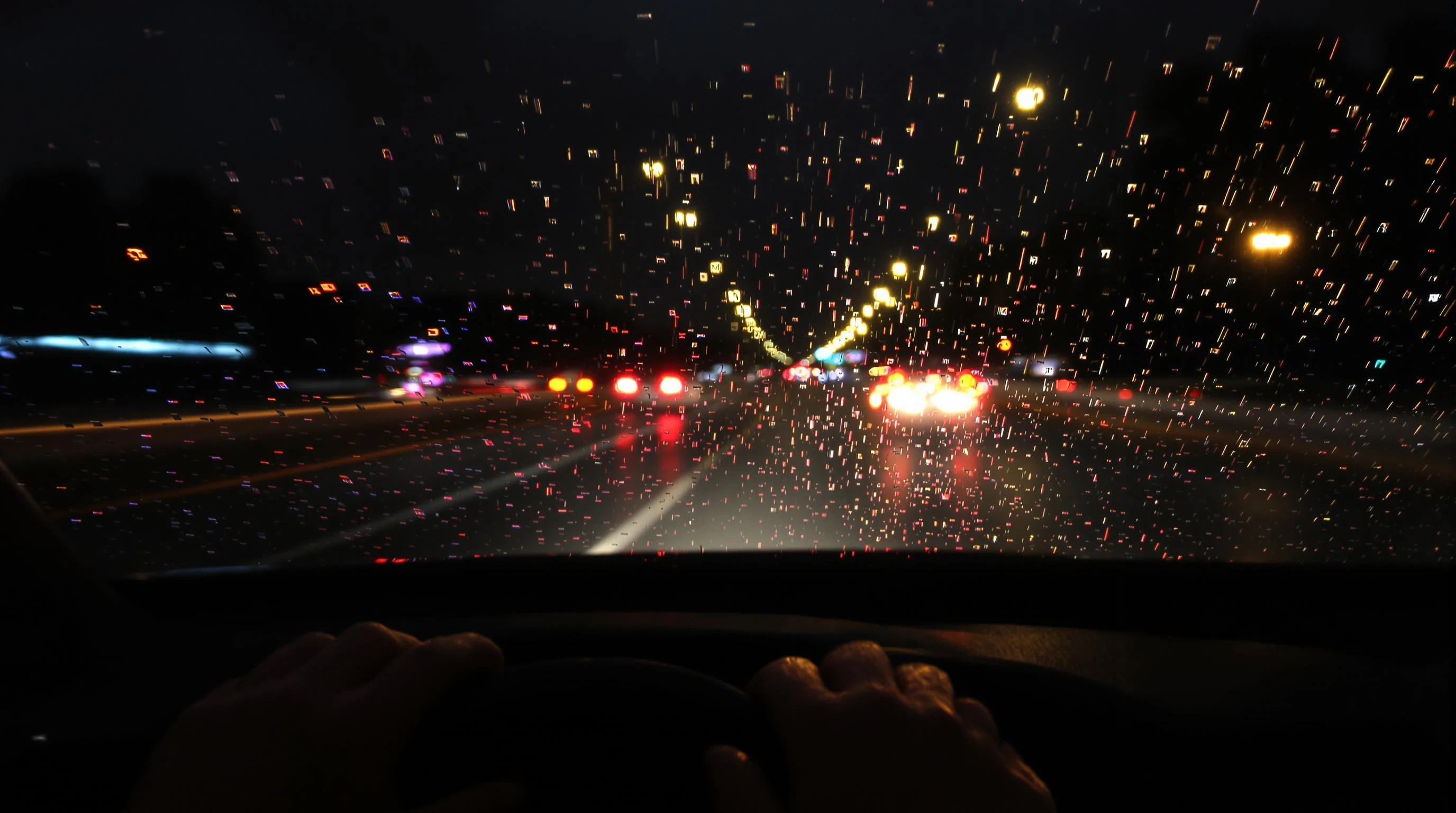 A realistic nighttime scene viewed from inside a moving car, showing blurred city lights through a rain-covered windshield. The road is illuminated by soft neon reflections and distant headlights. The dashboard is visible in the foreground, with a pair of hands on the steering wheel, suggesting calm and focus. The mood is cinematic, introspective, and peaceful – ideal for a night drive. Ultra-realistic, moody lighting, 4K photo quality, shallow depth of field.