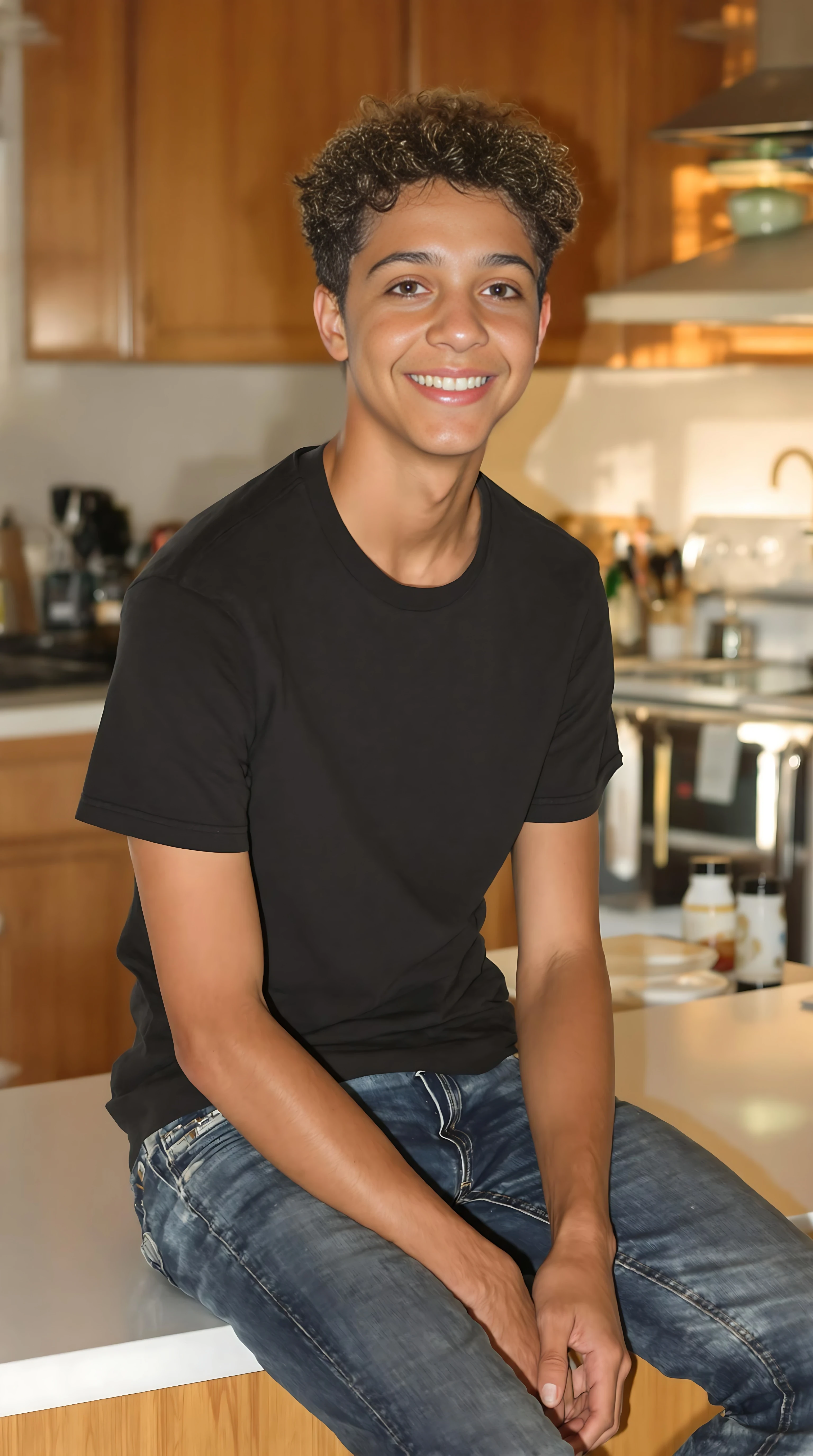 boring low quality snapchat photo circa 2015. A full body shot photo of a 16-year-old boy, sitting on the kitchen bench in his home kitchen, warmly lit in the late afternoon. The image is rich in detail, with warm tones and clear textures throughout. The boy has tanned skin, a medium, athletic build, brown curly hair and brown almond-shaped eyes. He is smiling subtly and warmly away from the camera as if someone is standing in front of him out of frame. He wears a black t-shirt, blue jeans and no shoes. The background features his home kitchen. The overall composition is balanced, with the young boy looking comfortable. The details are vivid, with textures of clothing, skin, and background elements clearly visible, while the warm lighting creates a relaxed and joyful mood