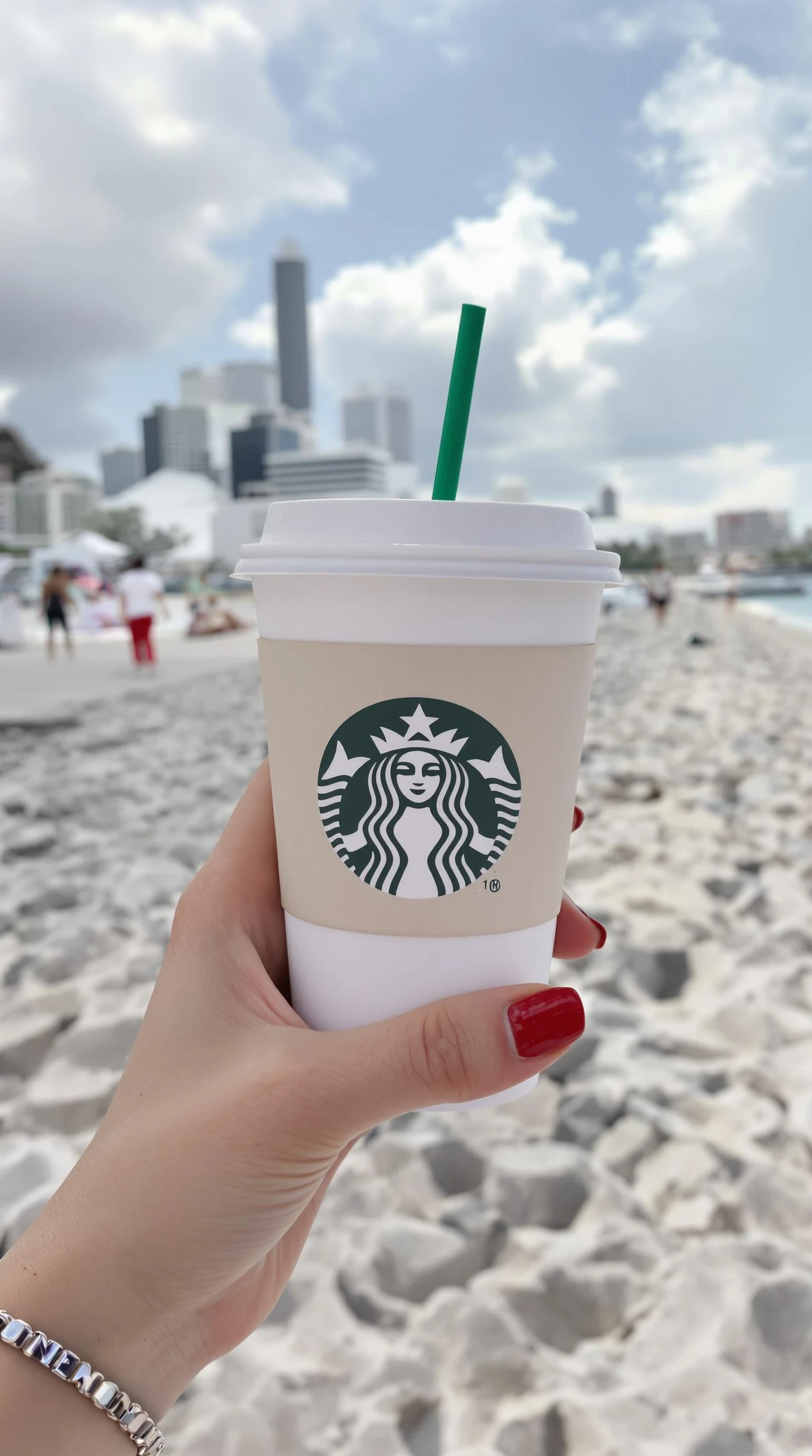 plain girl's hand holding starbuck coffee, red polished nails, at beach in miami,