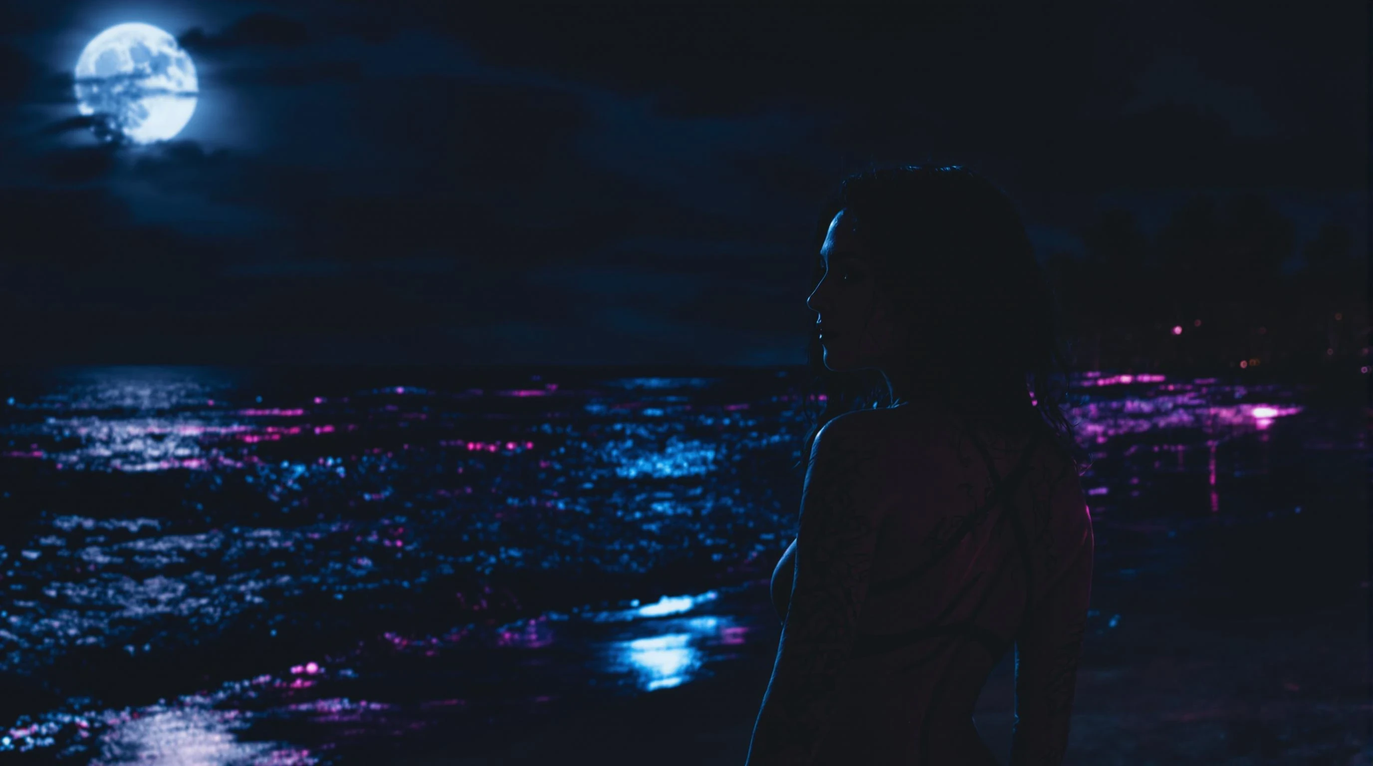 A stunning  image of a woman with tattoos looking sideways, set on a dark tropical beach at night. Strong moonlight and neon reflections. Empty space in the center for a logo overlay. Mystical, powerful, TrapNation-inspired. women is on the side of the image not in the centre.
