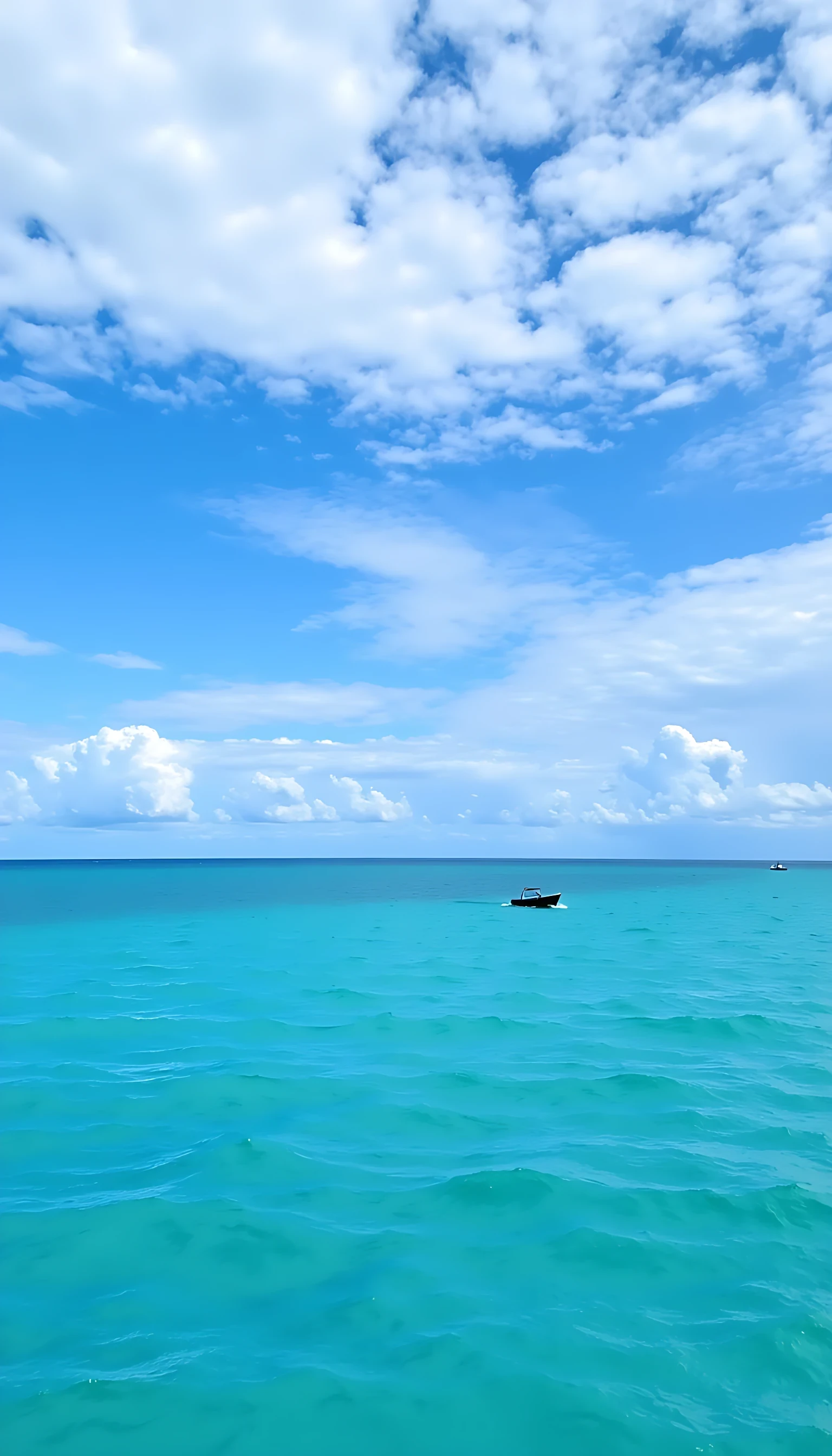 The image shows a beautiful blue ocean with two small boats in the distance. The sky is filled with white, fluffy clouds that are scattered across the horizon. The water is a deep turquoise color and the boats are small and black. The boats appear to be sailing on the water, with one boat in the foreground and the other in the background. The overall mood of the image is peaceful and serene.