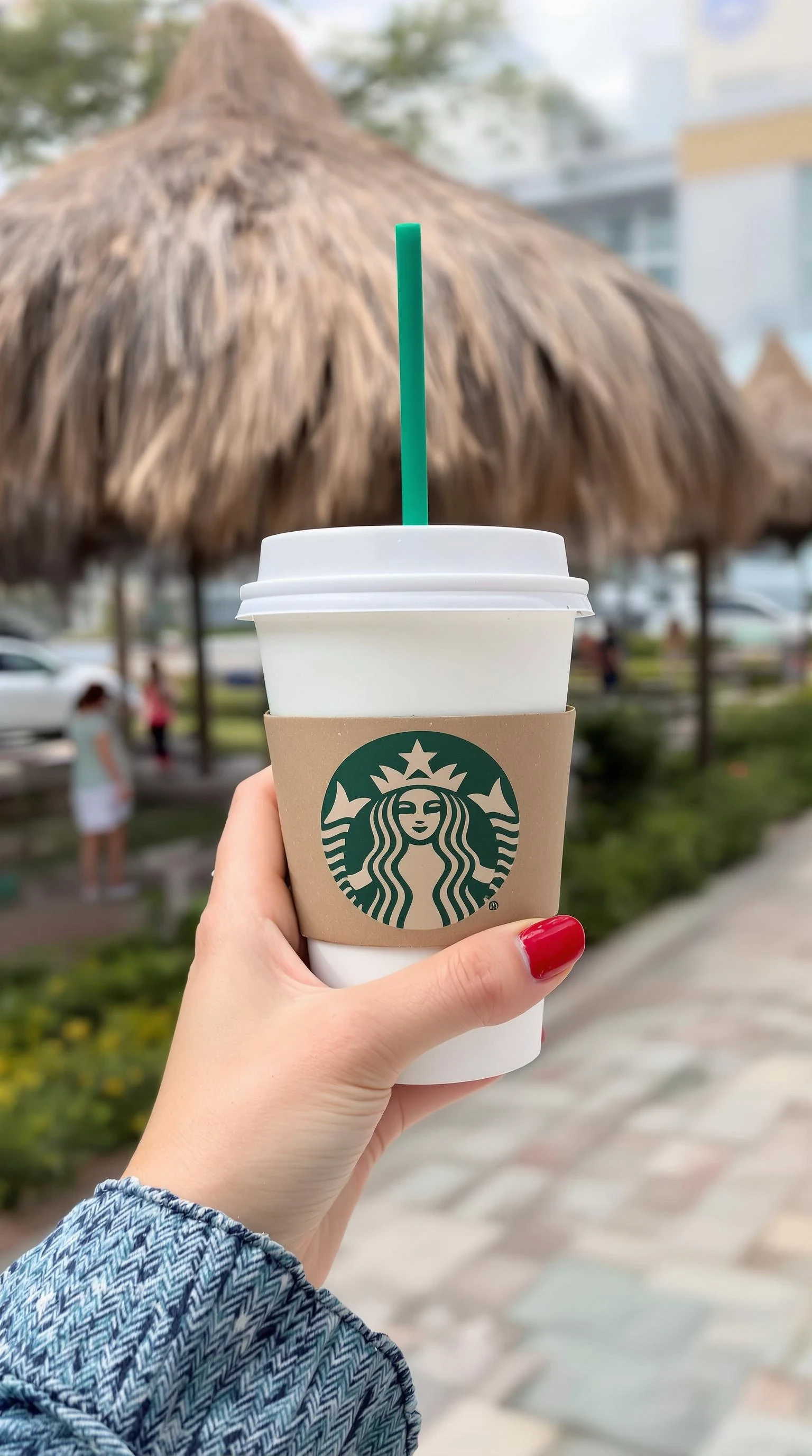 girl's hand holding starbuck coffee, red polished nails, at beach in miami