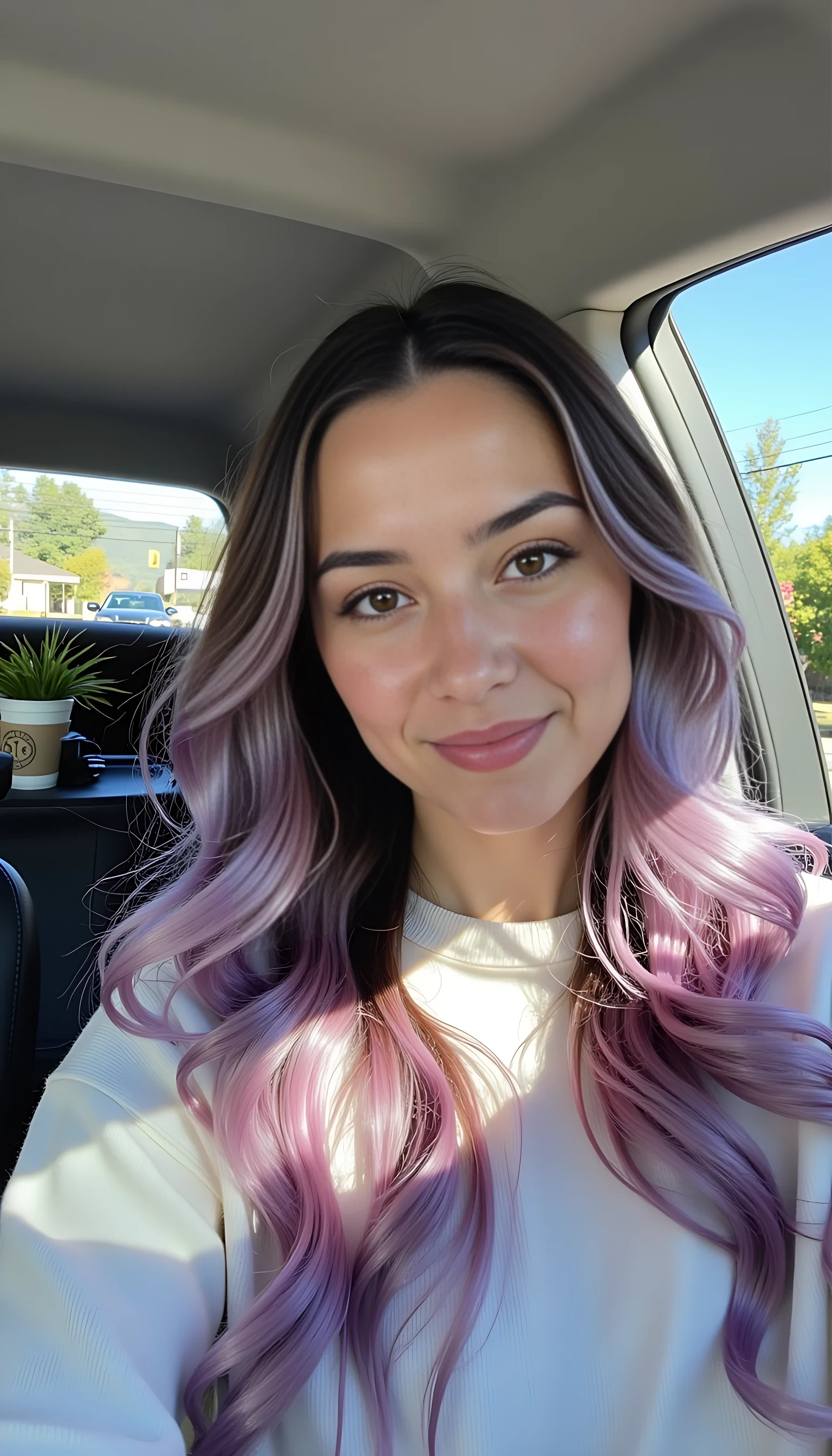 photo of woman CSTMDL, boring low quality snapchat photo circa 2015, A young woman with a warm smile, sitting in the driver's seat of a cozy car. She has soft, Long wavy dark purple hair with pink ombre. cascading past her shoulders. The sunlight streams through the window, casting a gentle glow on her face. The interior of the car is neat and comfortable, with a coffee cup in the cup holder and a small plant on the dashboard. The background outside the window shows a scenic road lined with trees and blue skies