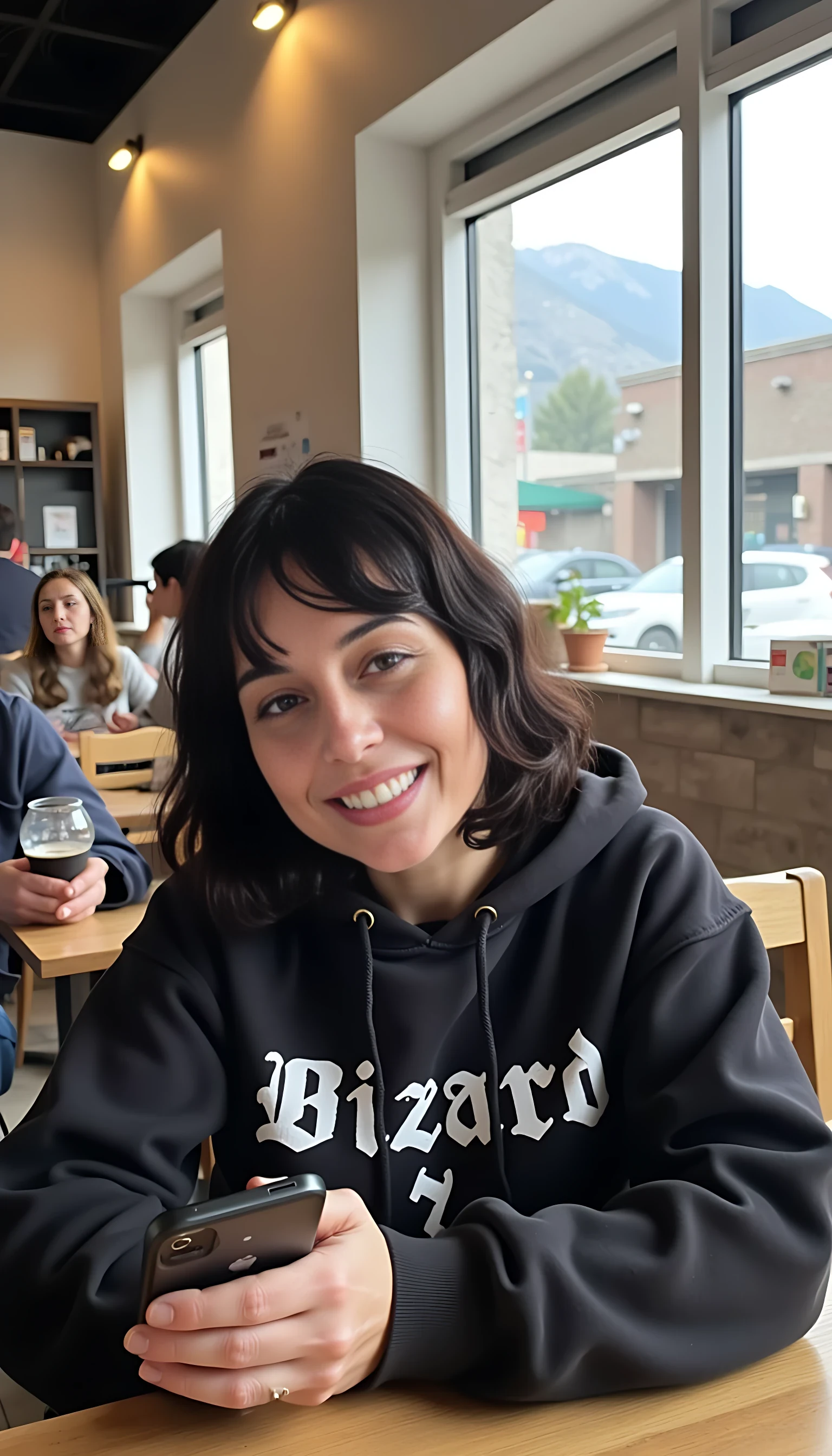 iphone portrait of CSTMDL woman younger Bob length hair hair makeup bangs cute smile brown eyes and sitting in cafe holding phone in busy restaurant wearing hoodie says “wizard”  mountains background shopping bags 
