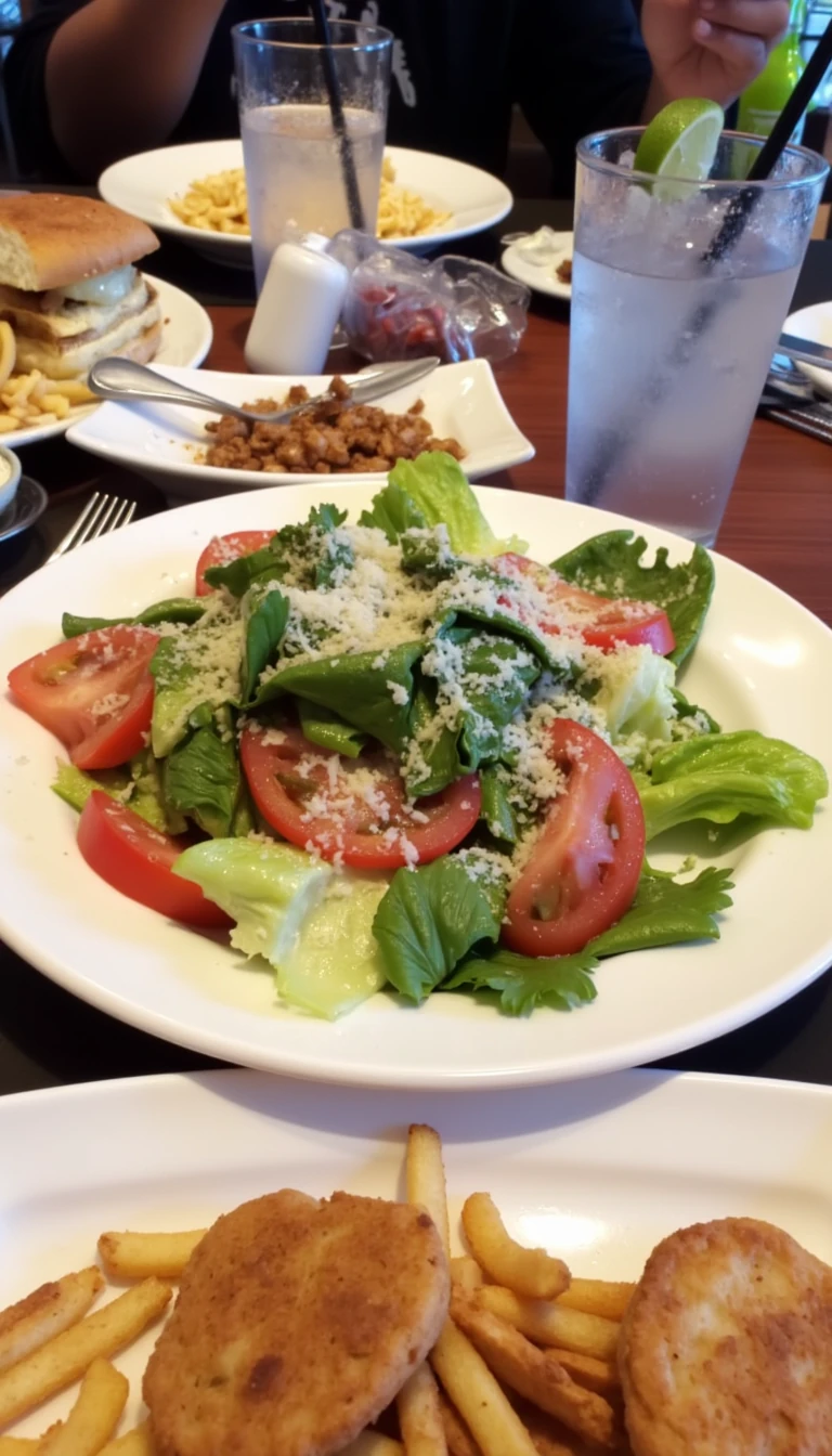 boring low quality snapchat photo circa 2015, this picture is being taken in a restaurant. The picture is of large salad with a glass of water next to it. There are other food dishes and drink glasses on the table as well.  All the food dishes are white.