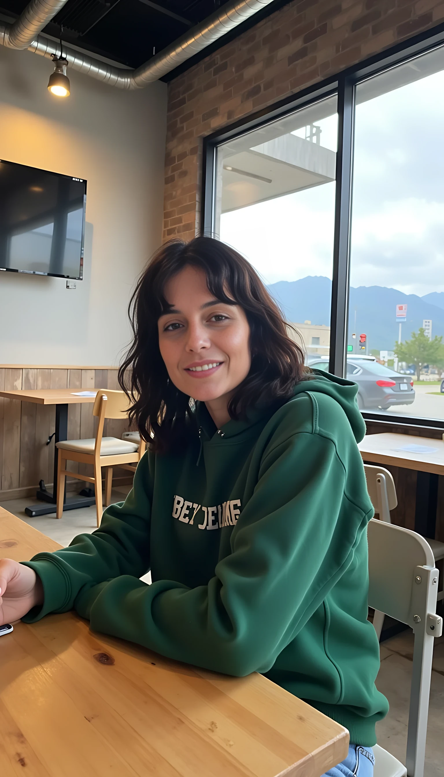 iphone portrait of CSTMDL woman younger Bob length hair hair makeup bangs cute smile brown eyes and sitting in cafe holding phone in busy restaurant wearing green hoodie and shorts mountains background 
