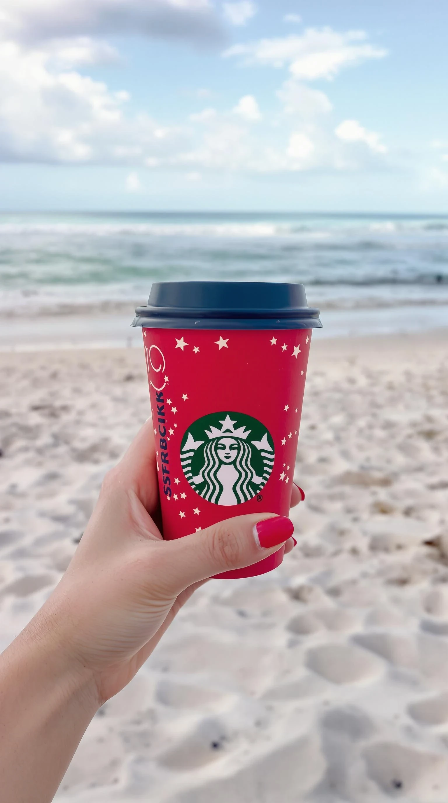 plain girl's hand holding starbuck coffee, red polished nails, at beach in miami,