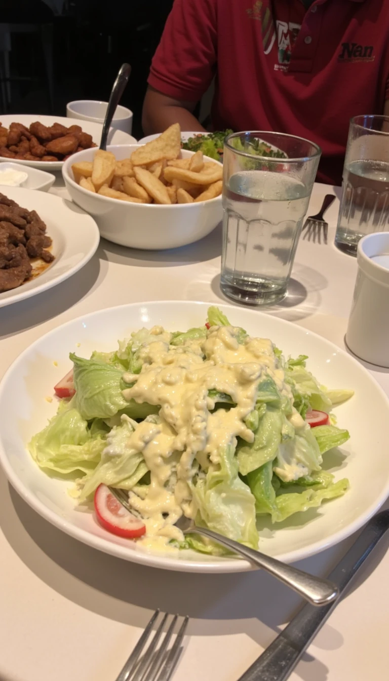 boring low quality snapchat photo circa 2015, this picture is being taken in a restaurant. The picture is of large caesar salad with a glass of water next to it. There are other food dishes and drink glasses on the table as well.  All the food dishes are white.