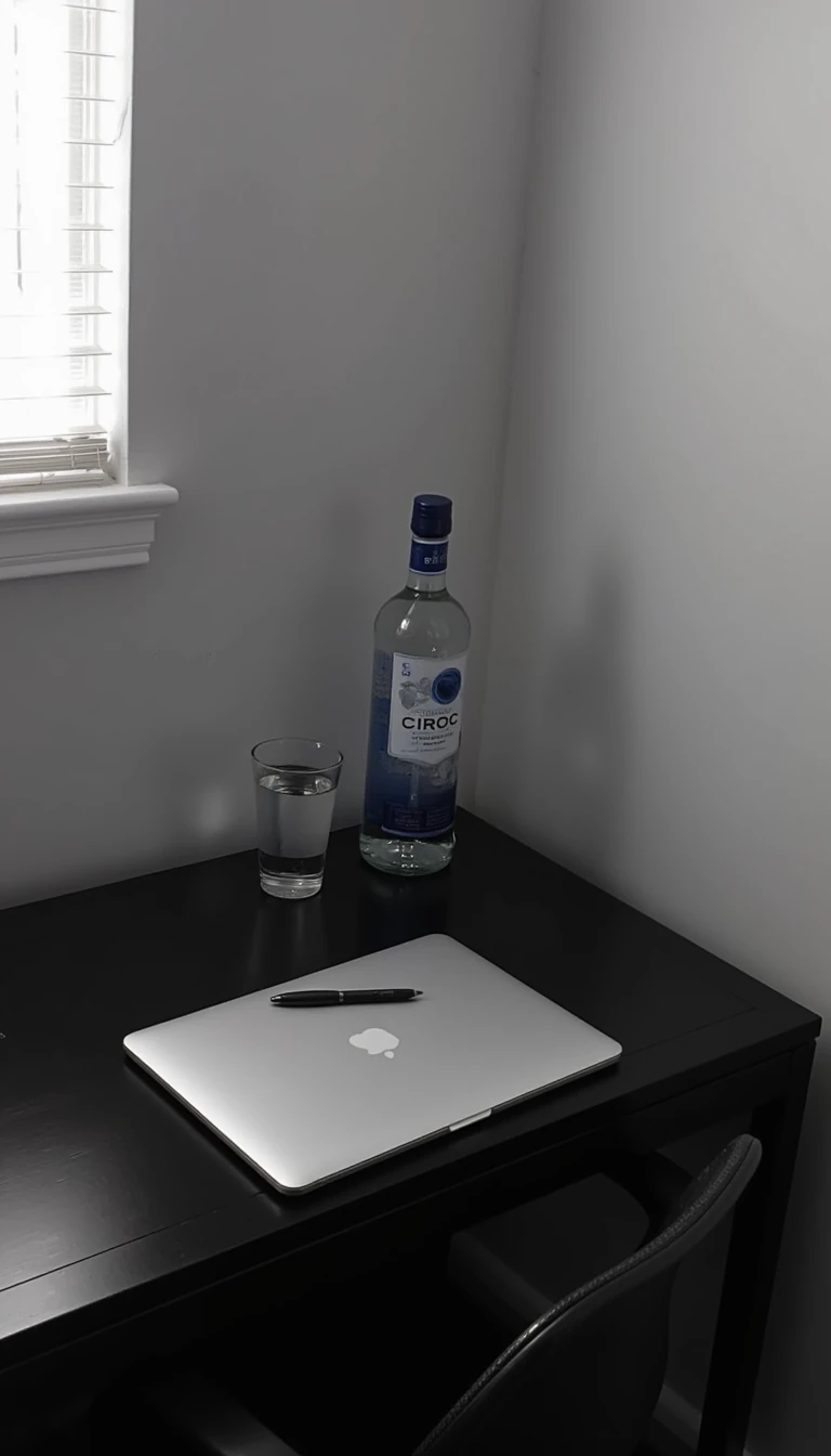 boring low quality snapchat photo circa 2015, this picture is being taken of a black desk in the corner of a room touching the grey walls to the right of the desk and behind the desk. The desk has an all black pen, a macbook air, bottle of ciroc vodka and a glass of water on it. 