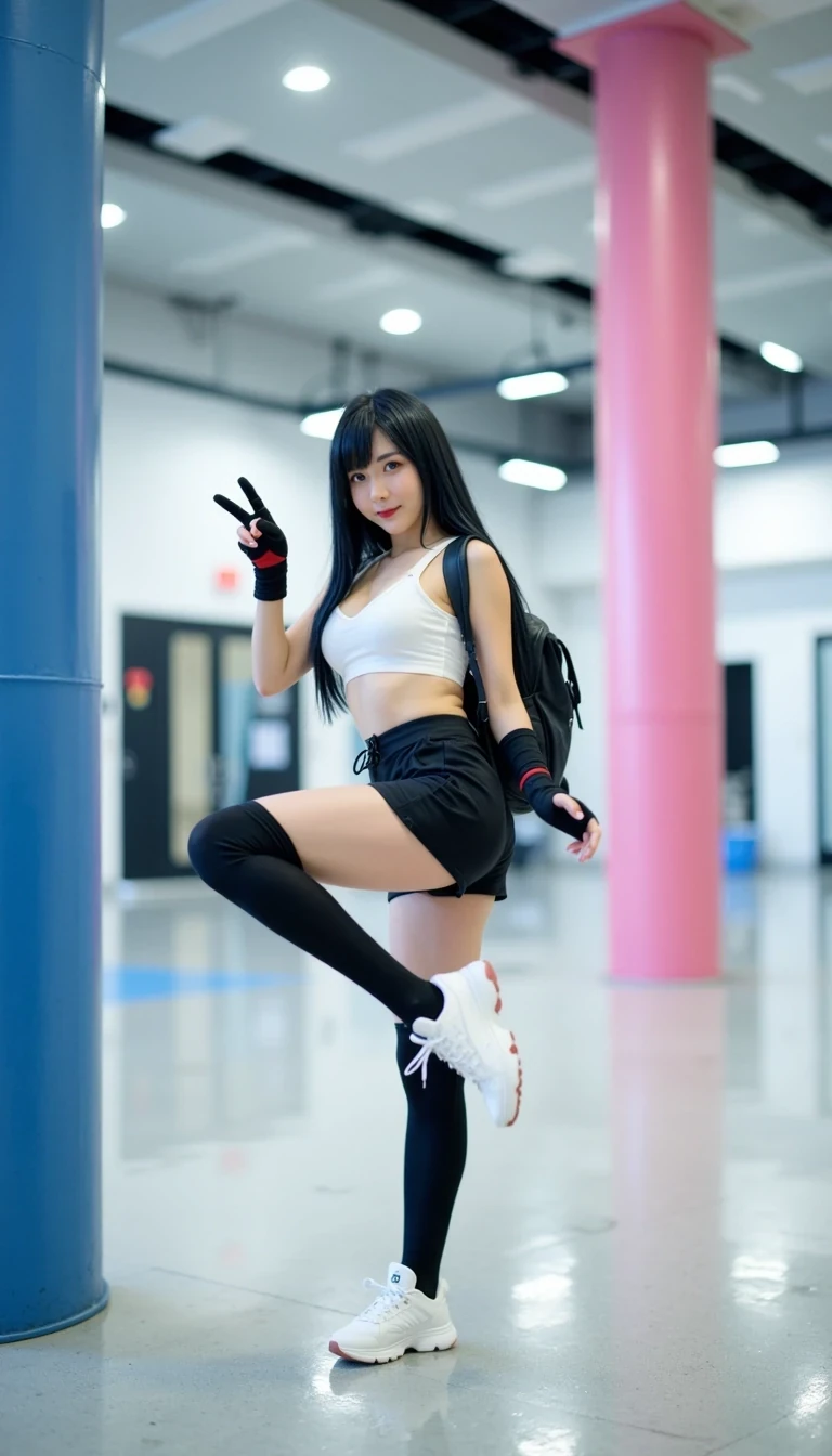 This photograph captures a young woman performing a high kick in a modern, well-lit indoor space, possibly a gym or convention hall. She has long, straight black hair with bangs, and is wearing a cosplay outfit inspired by Final Fantasy VII's character, Tifa Lockhart. The costume includes a white sports bra, black shorts, black thigh-high socks, and white sneakers. Her outfit is accessorized with black fingerless gloves and red wristbands, and she carries a black backpack slung over her shoulders.

Her skin is fair, and she has a slender, toned physique with large breasts. She is smiling and making a peace sign with her right hand, adding a playful and energetic vibe to her pose. Her left leg is extended high, showcasing her flexibility and agility.

The background features a clean, modern interior with a high ceiling and recessed lighting, providing a bright, even illumination. There are two large cylindrical pillars, one in blue and the other in pink, which likely serve as support structures or decor. The floor is a polished, light gray surface that reflects the surroundings. The overall ambiance is modern and sleek, emphasizing the clean lines and bright, open space.
