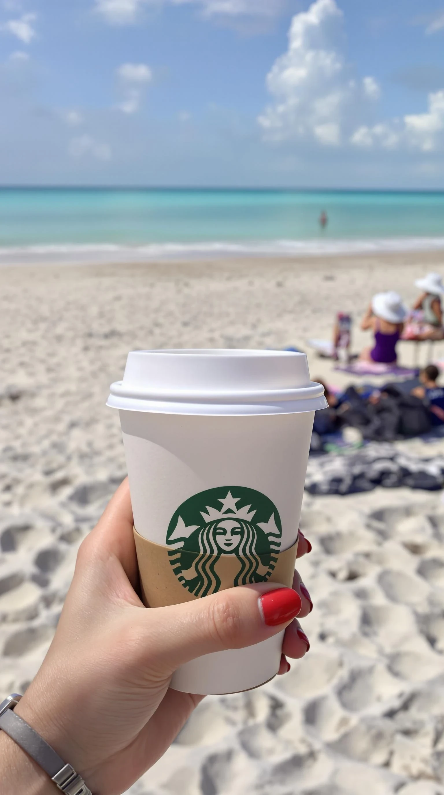plain girl's hand holding starbuck coffee, red polished nails, at beach in miami,