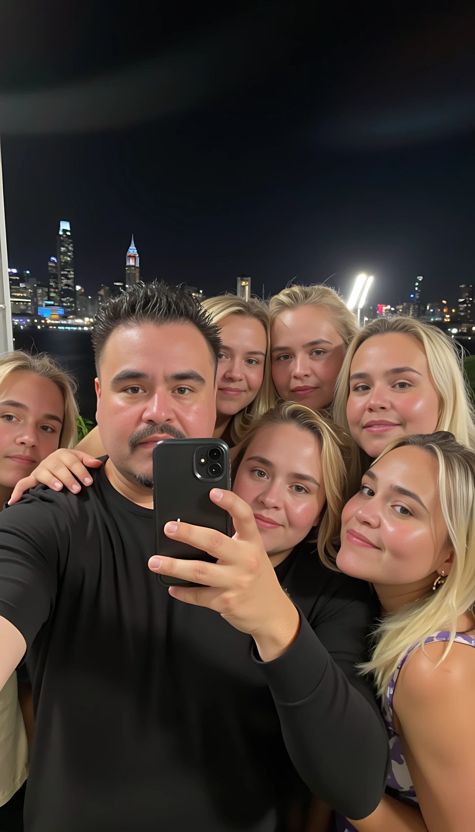 Selfie in a  mirror full man body wearing a  nice black dress shirt   Hugging with 5 blonde girls with blue eyes in a  big city night lights background 
