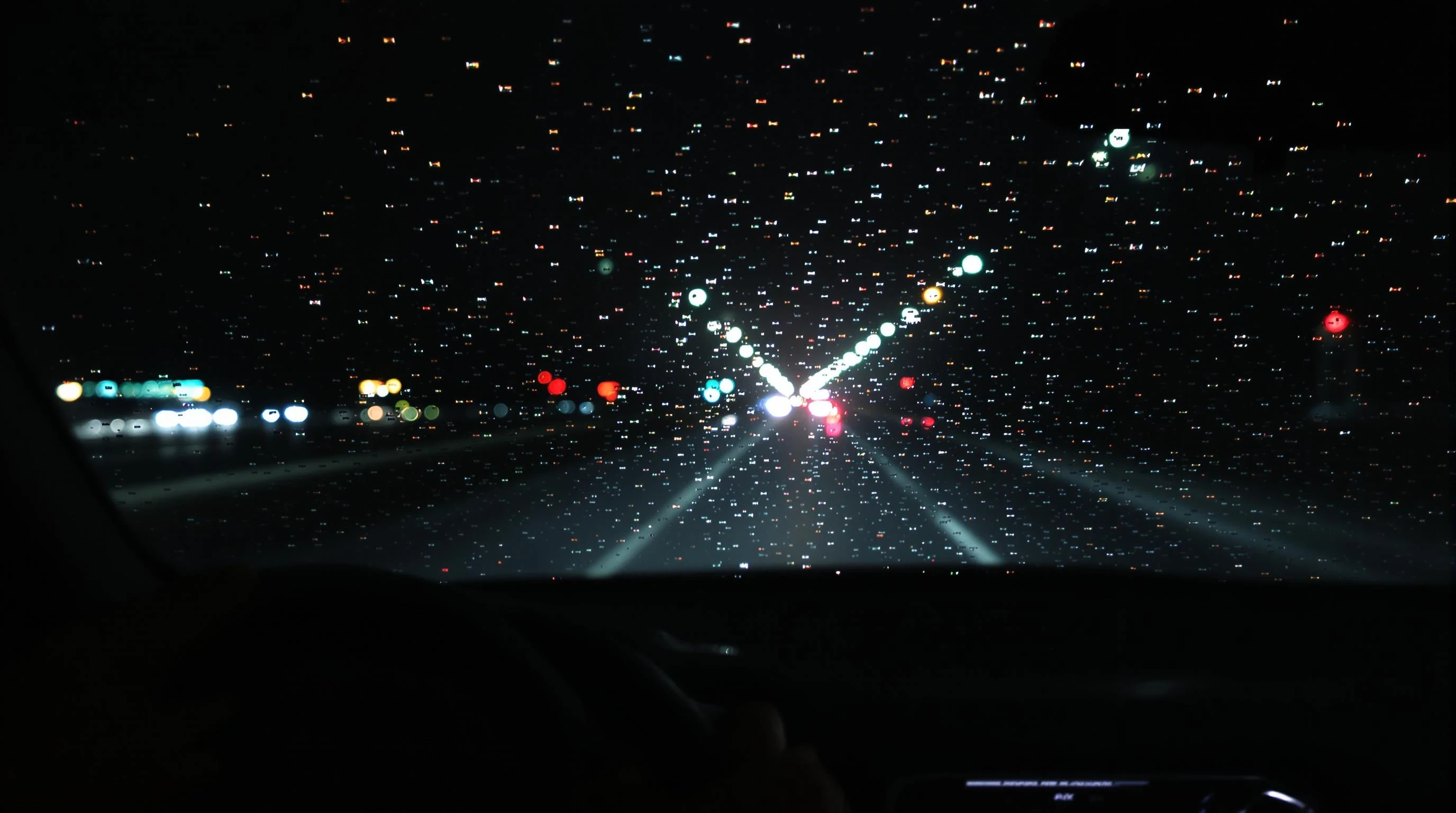 "A realistic nighttime scene viewed from inside a moving car, showing blurred city lights through a rain-covered windshield. The road is illuminated by soft neon reflections and distant headlights. The dashboard is visible in the foreground, with a pair of hands on the steering wheel, suggesting calm and focus. The mood is cinematic, introspective, and peaceful – ideal for a night drive. Ultra-realistic, moody lighting, 4K photo quality, shallow depth of field."