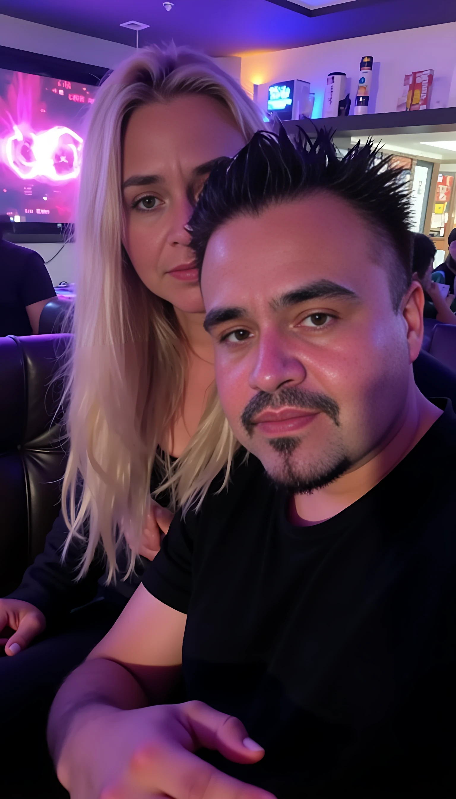 Man full average body with a beautiful blonde woman with blue eyes seating on his lab and a couch  with a night club background 